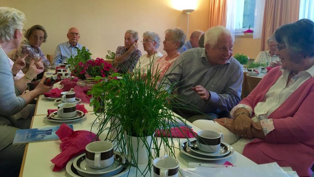 Ältere Menschen sitzen zusammen am geschmückten Kaffeetisch
